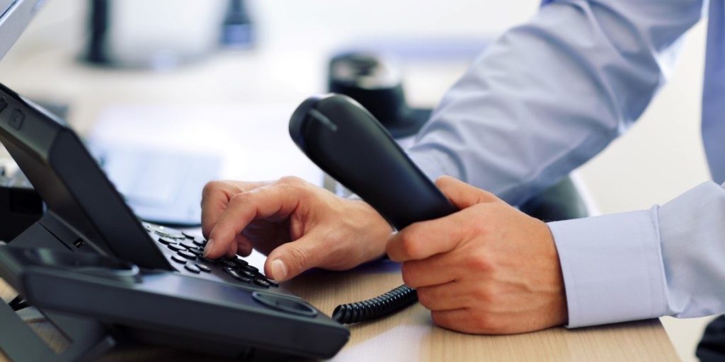 A man is using a telephone on a desk.