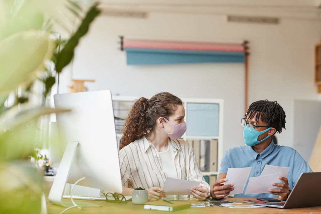 Two people wearing face masks at a desk.