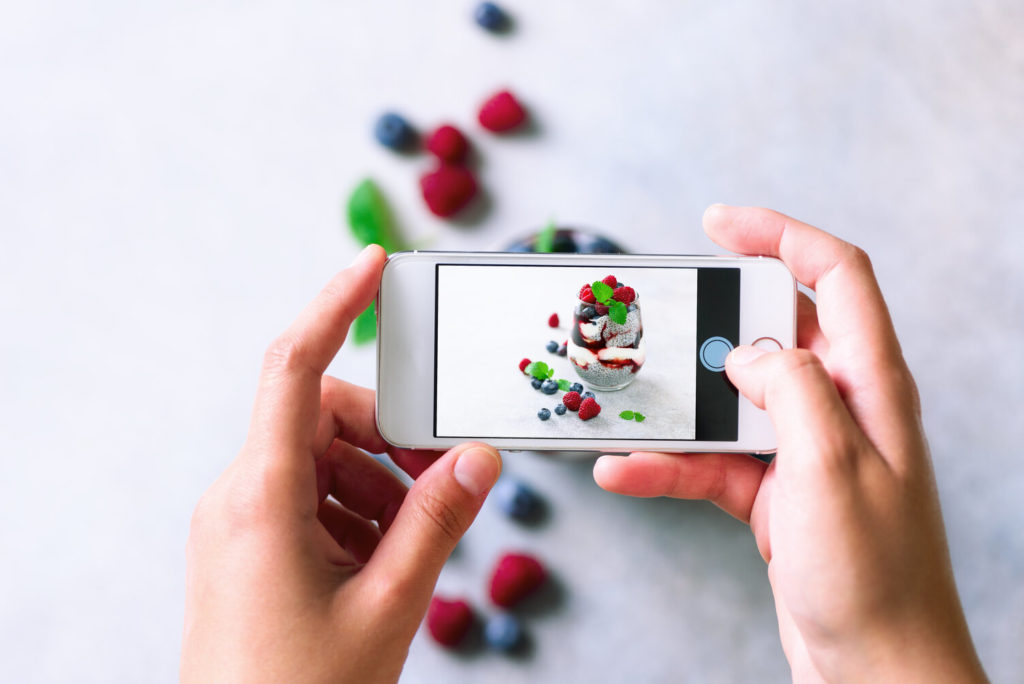 Girl taking photos of breakfast, chia pudding with berries to mobile phone for Social Media