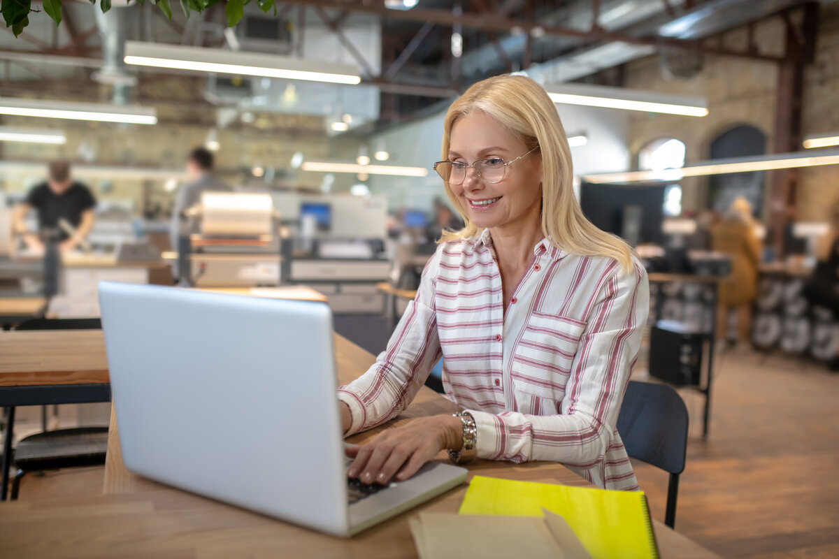 At work. Blonde woman sitting in workshop, typing on laptop