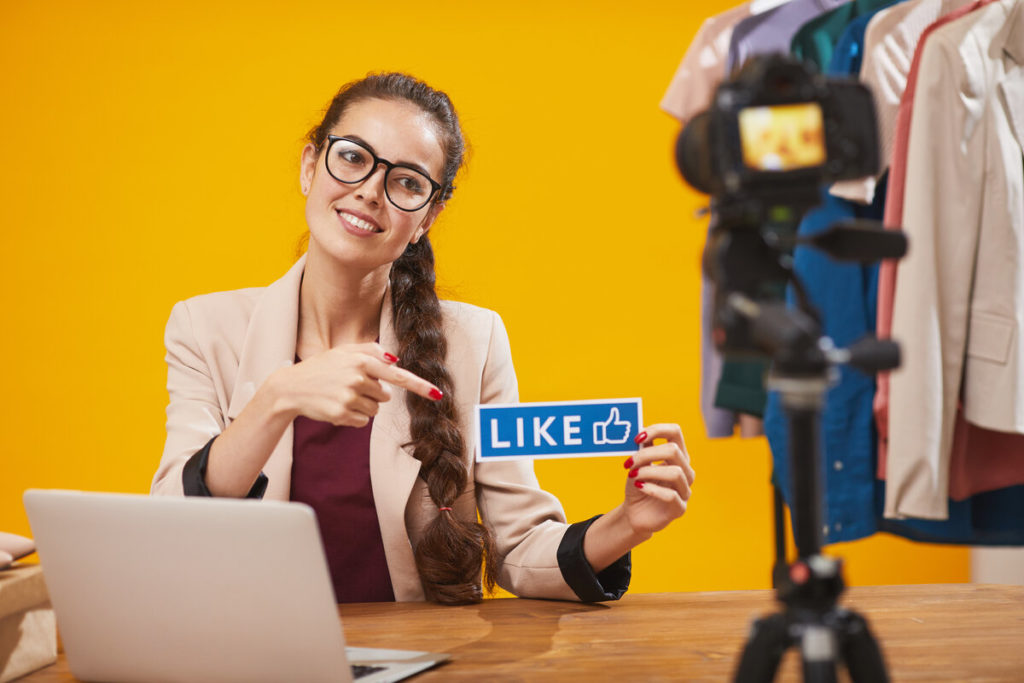 Portrait of contemporary young woman holding LIKE word and smiling at camera while filming video for beauty and lifestyle social media channel
