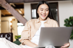 Happy asian woman resting at home with laptop, watching videos or browsing a site on computer