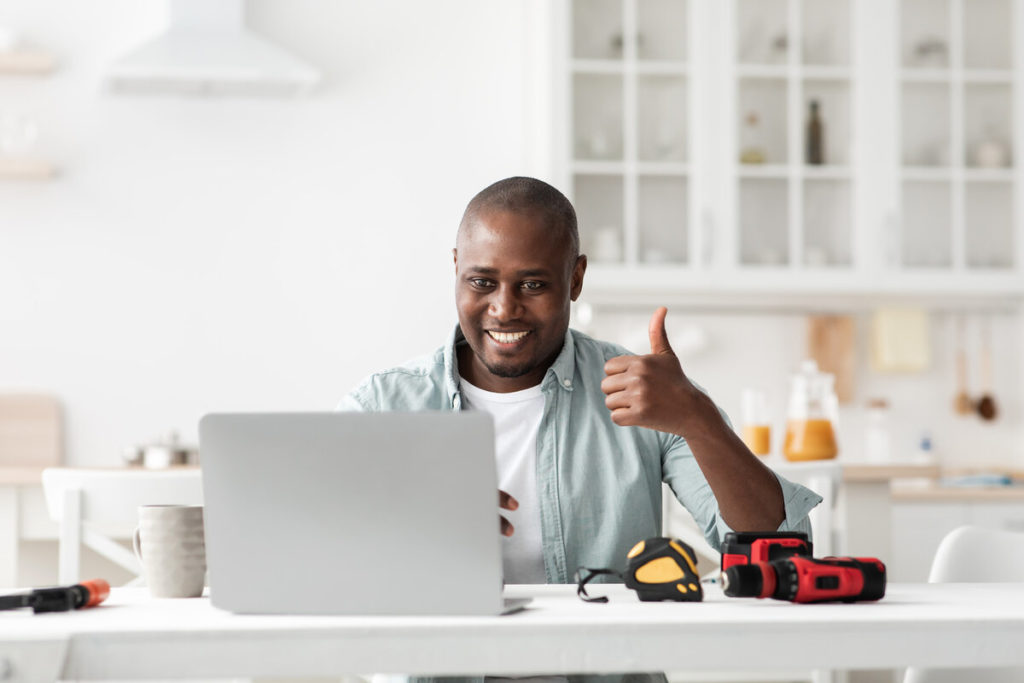 reputation marketing plan review of construction instruments. Happy black handyman looking at laptop webcam and showing thumb up