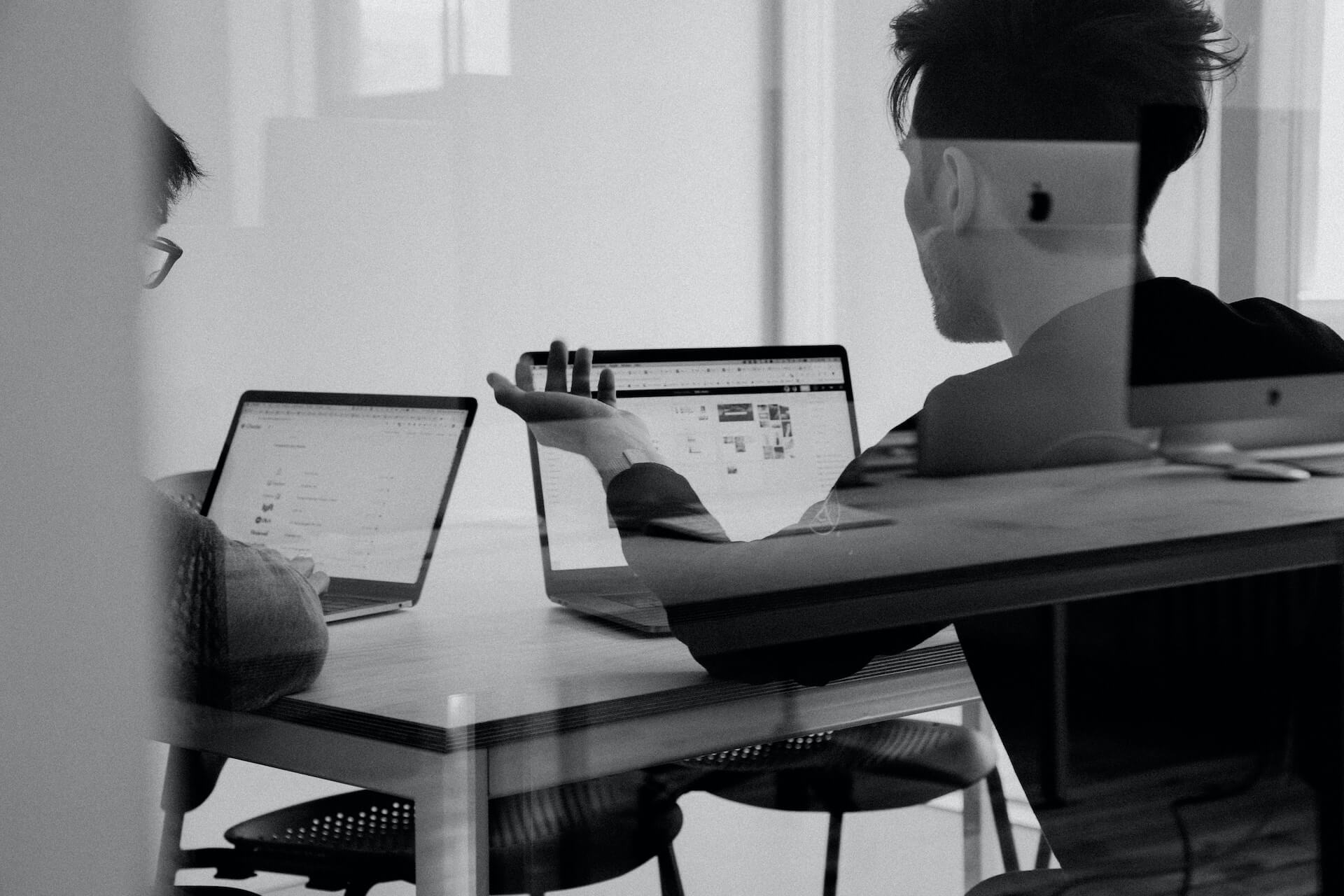 Two people sitting at a desk with laptops in front of them.