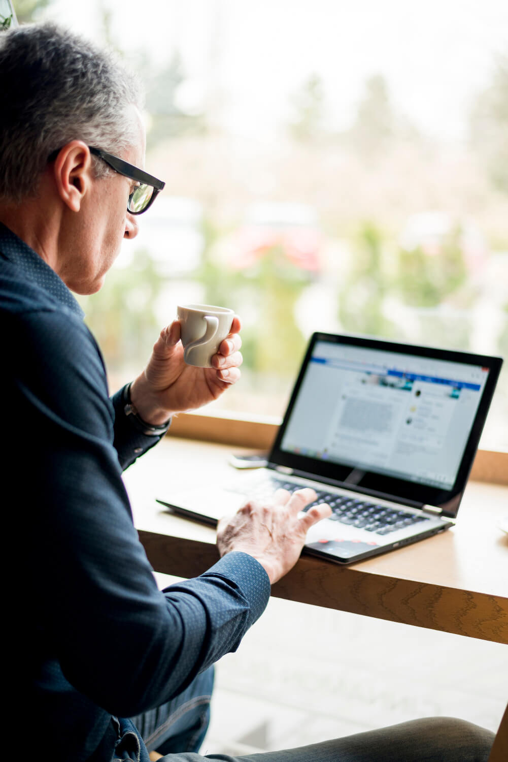 A man sitting at a table with a laptop and a cup of coffee.