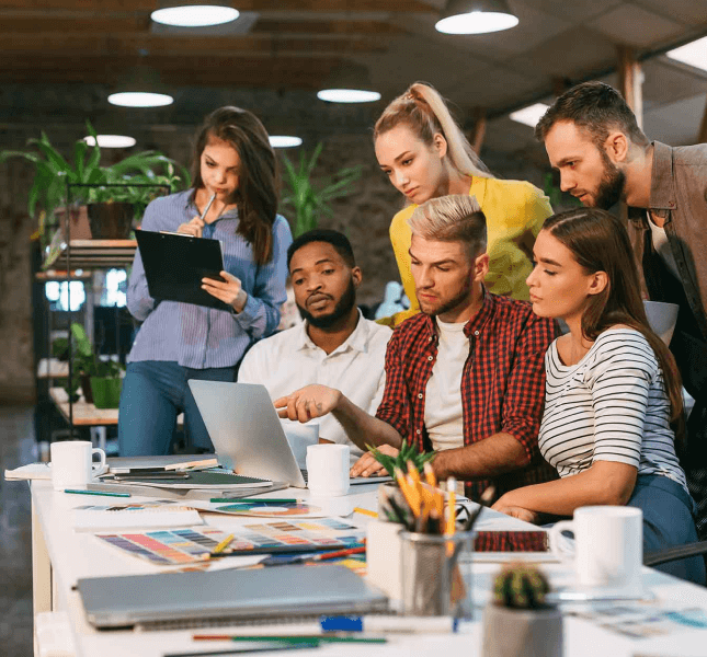 A group of people looking at a laptop in an office.