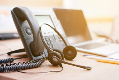 A phone and headset on a desk next to a laptop.