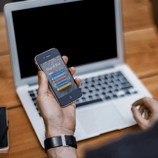 A man holding a cell phone in front of a laptop.