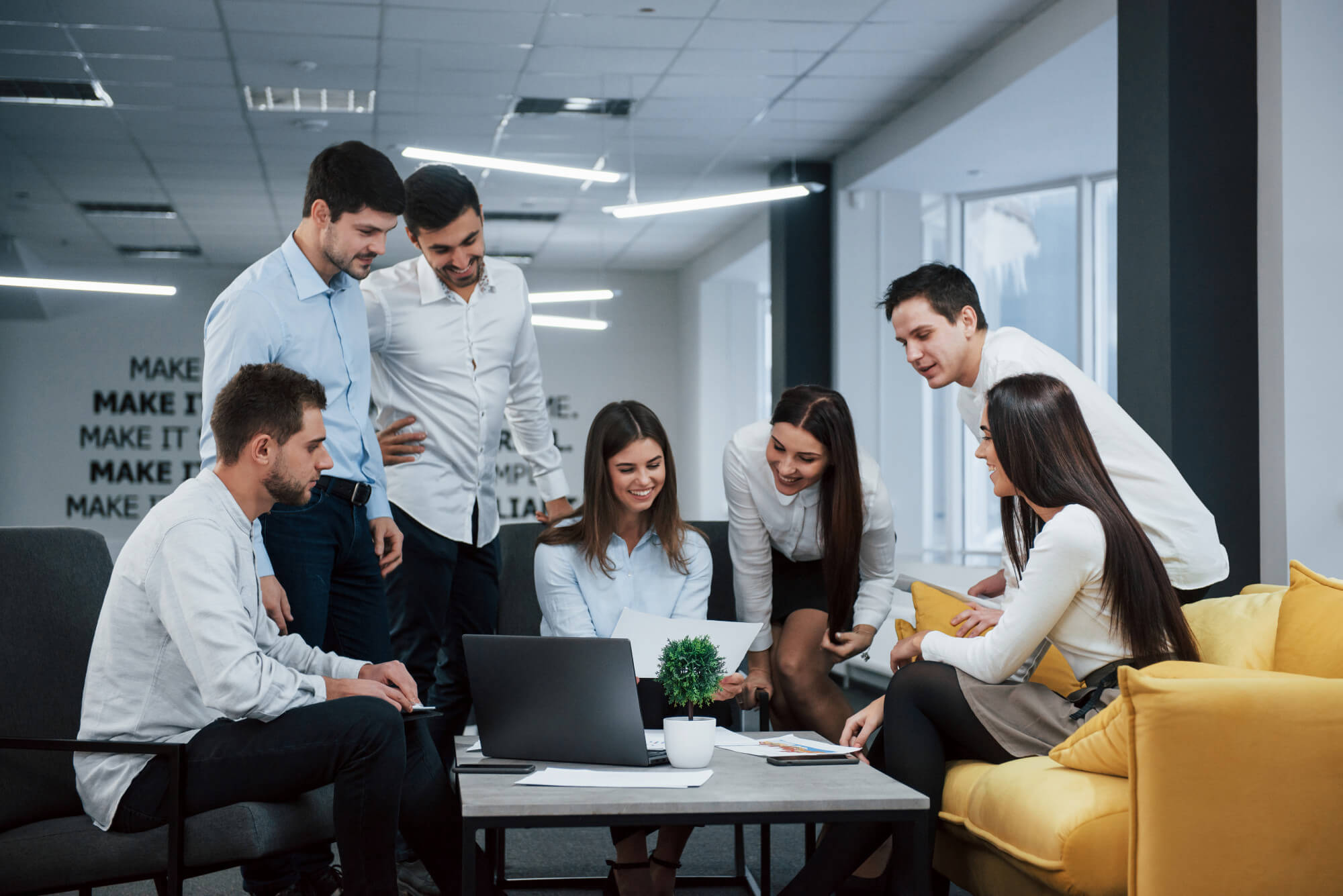 A group of people sitting around a yellow couch in an office.