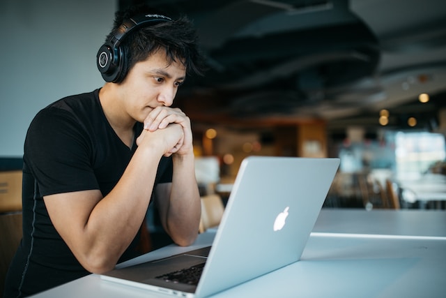 A man wearing headphones is sitting at a table with a laptop.